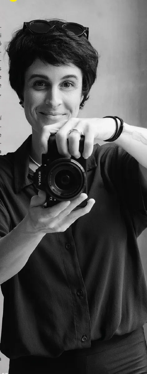 Retrato en blanco y negro de Ailin Beller sonriendo con una cámara en las manos