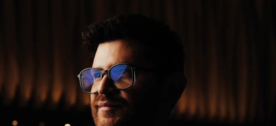 Elias Rivero con lentes, iluminado en tonos cálidos dentro de un bar