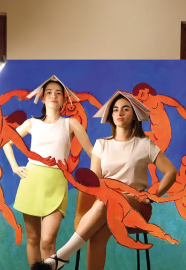Paula Pérez y Belinda Chnaid frente a un mural con figuras naranjas