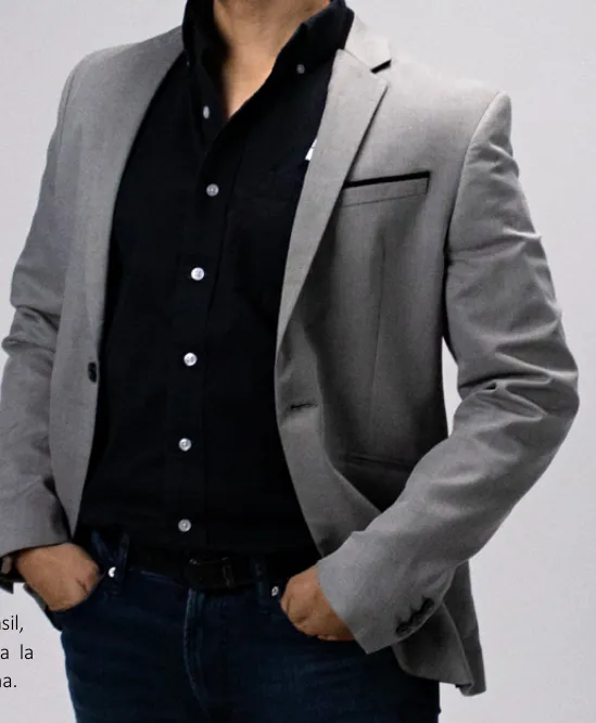 Roberto Mena de pie con saco gris y camisa negra, con la mano en el bolsillo