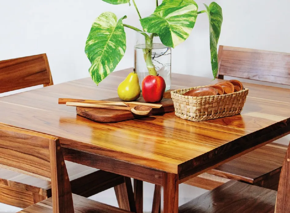 Mesa de comedor de madera de teca con frutas, canasta tejida y una planta en jarrón